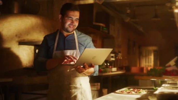 在餐厅: 英俊的男厨师使用笔记本电脑。正宗披萨店烹饪美味的有机生态食品。在小型企业家庭商店从事在线订