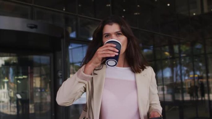 白人女商人在现代办公室外使用智能手机并喝外卖咖啡