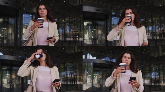 白人女商人在现代办公室外使用智能手机并喝外卖咖啡