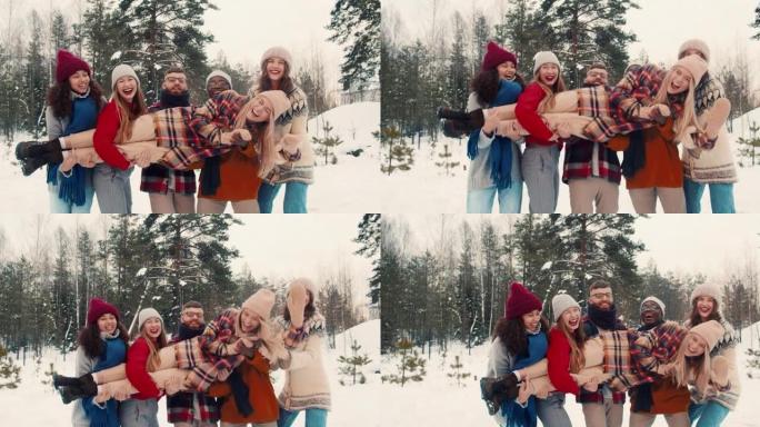 有趣快乐的多民族朋友举行，摇滚年轻金发女子在白雪皑皑的森林圣诞假期慢动作中大笑。