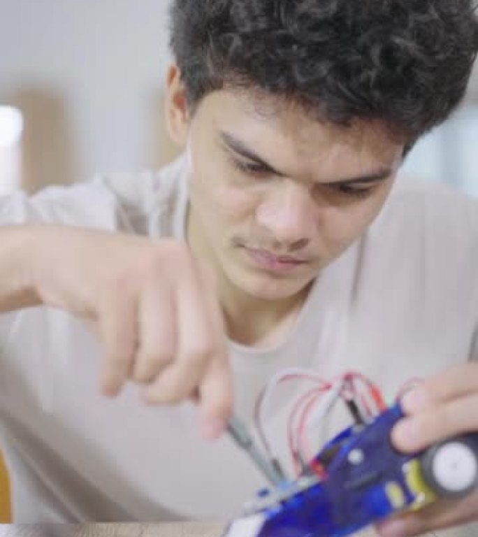 一个高中生用螺丝刀集中注意力修理他的机器人汽车的特写镜头。