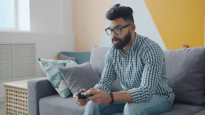 混合种族男子的慢动作享受电子游戏在公寓的沙发上放松
