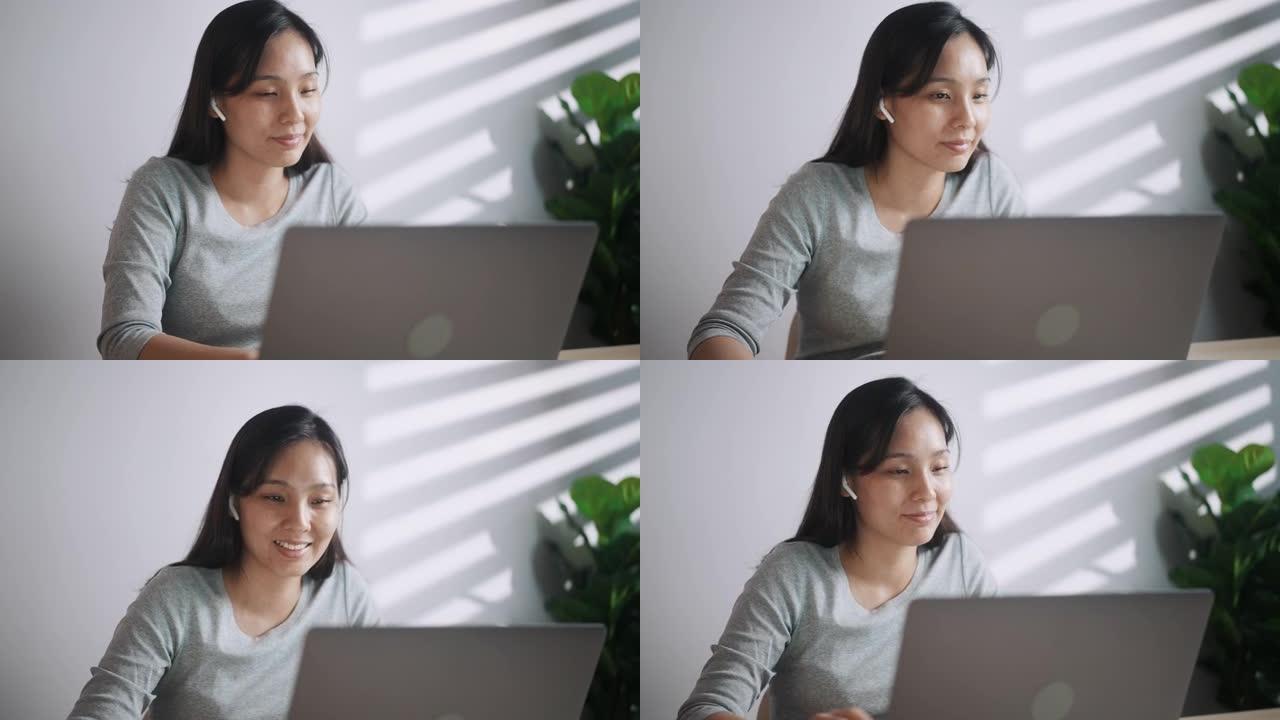微笑着迷人的年轻女子在笔记本电脑上打字坐在桌子旁