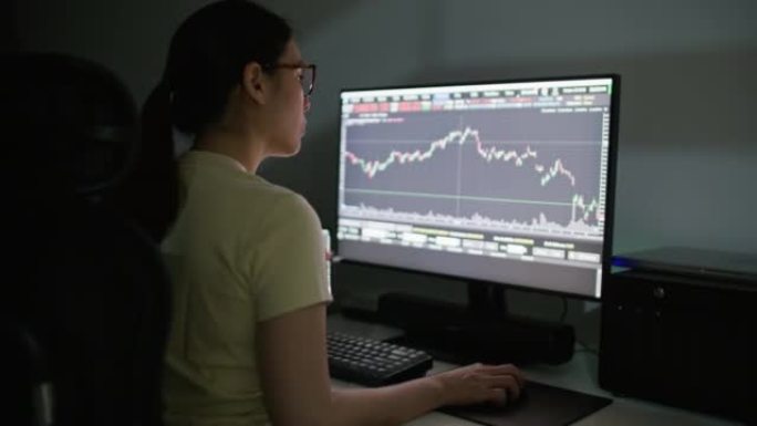 集中亚洲女性坐在台式电脑附近，使用电脑屏幕在家投资股市数据