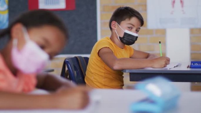 上课期间坐在教室里的高加索男生的肖像，戴着口罩做笔记