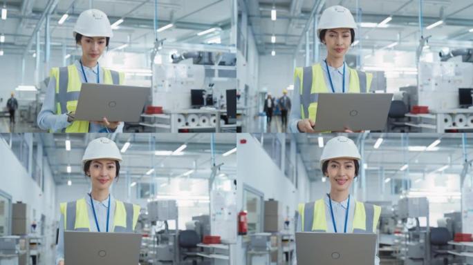 电子制造厂一位戴着白色安全帽的快乐微笑的亚洲女工程师的肖像，站在笔记本电脑上。成功的员工摆姿势拍照。