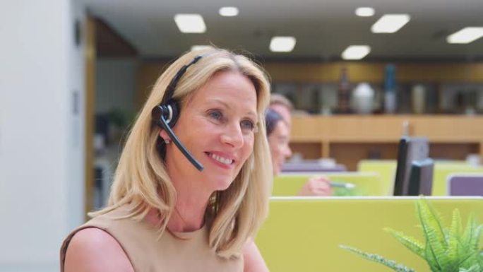 成熟的女商人戴着电话耳机与客户服务中心的呼叫者通话