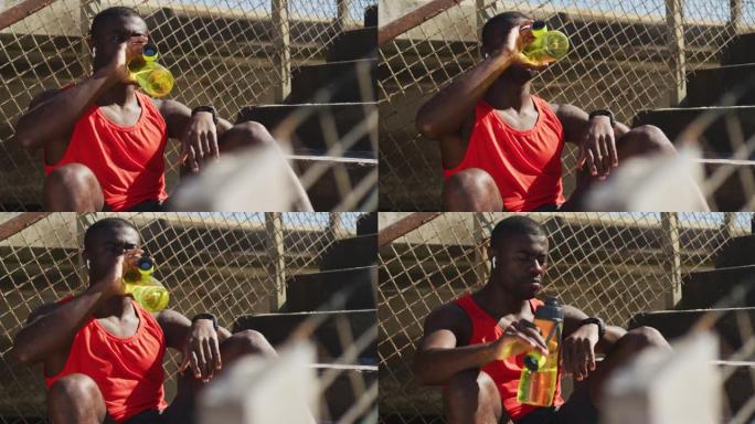 疲惫的非洲裔美国男子坐着，用水瓶喝水，在户外锻炼休息