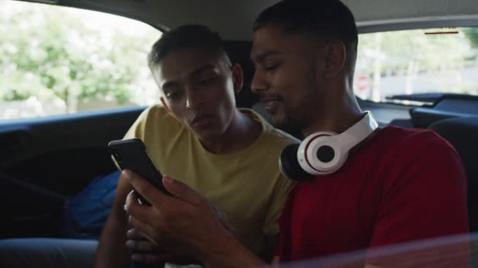 两个快乐的混血朋友拿着咖啡，在出租车上使用智能手机