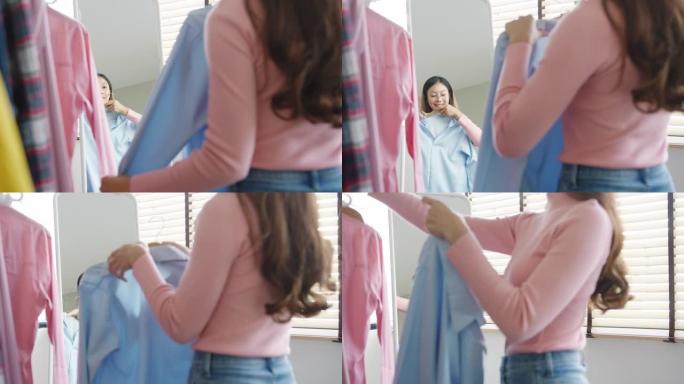 美丽迷人的亚洲女士在衣架上选择衣服，穿着照镜子，在家里的卧室里。