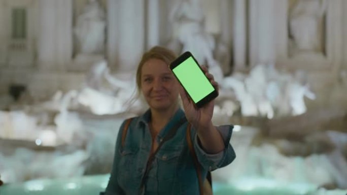 SLO MO游客晚上在特雷维喷泉 (Trevi Fountain) 展示带有绿屏的智能手机