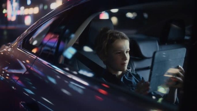 小男孩坐在汽车后座上，晚上通勤回家。乘客在平板电脑上观看有趣的娱乐活动，同时在城市街道上乘坐出租车，