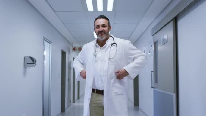微笑的白人男性医生的肖像穿着实验室外套站在医院走廊上