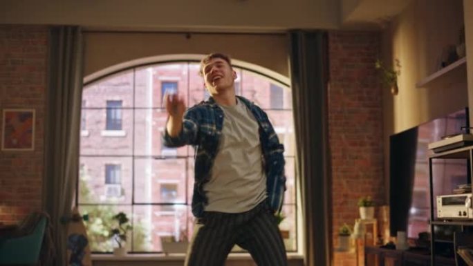 快乐英俊的年轻人穿着休闲装跳舞，在阁楼公寓里独自享受时光的肖像。为社交媒体录制有趣的病毒视频。