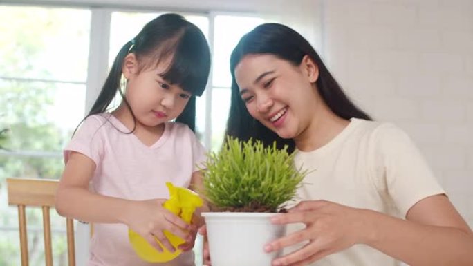 快乐快乐的亚洲家庭妈妈和女儿在家里窗户附近的园艺植物上浇水。