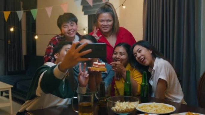 一群年轻的亚洲朋友与生日蛋糕看相机拍摄视频照片在移动应用程序有趣的视频聚会在夜生活室内家庭。