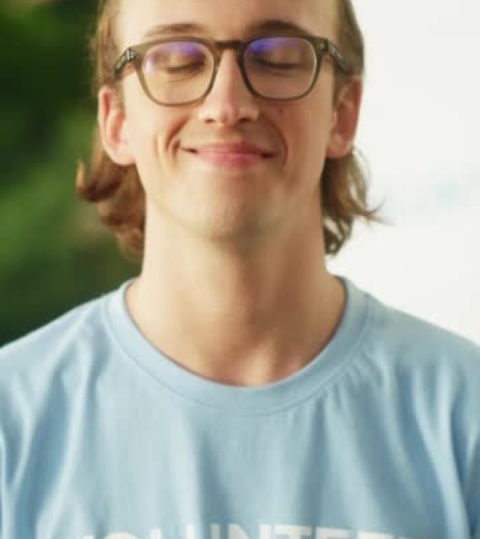一位有吸引力的年轻男性志愿者的垂直肖像。戴着眼镜的快乐高加索人，穿着蓝色t恤，微笑着看着相机。人道主