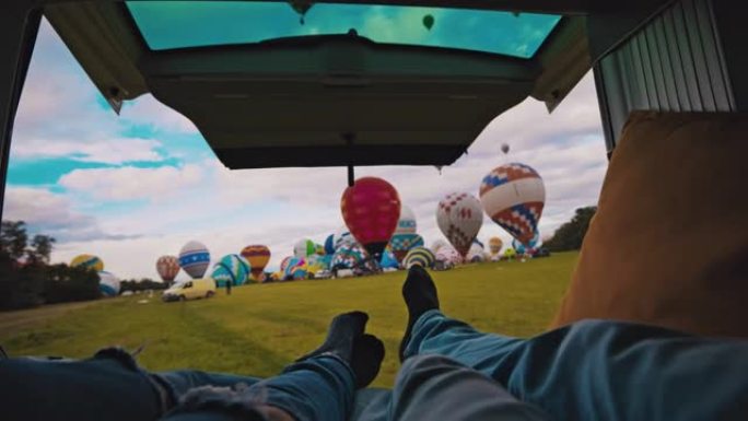 POV夫妇躺在货车上，看着农村地区的热气球
