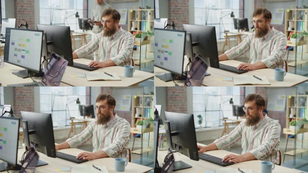 年轻的高加索大胡子男子的肖像，戴着眼镜，在明亮宽敞的办公室里坐着在电脑上工作时微笑。男性法律顾问在键