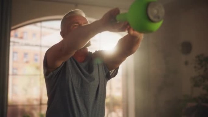 强壮的运动健美的中年男子举起和摆动沉重的壶铃，在阳光明媚的公寓的家中进行晨练时进行核心强化锻炼。健身