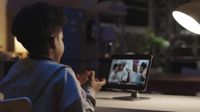后视图，9岁的非洲民族快乐男孩庆祝生日，圣诞节在社交距离期间与亲戚的家人一起在家里使用平板电脑上的网