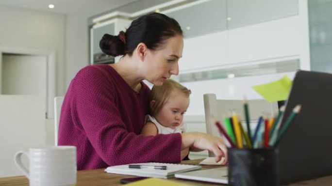 白人母亲在家工作时用笔记本电脑抱着婴儿