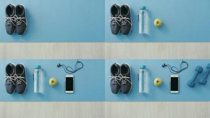 平坦地从瑜伽垫上的健身器材上方面对蓝色的复制空间。跑步者，水瓶，手机，耳机，哑铃和苹果健康均衡饮食，