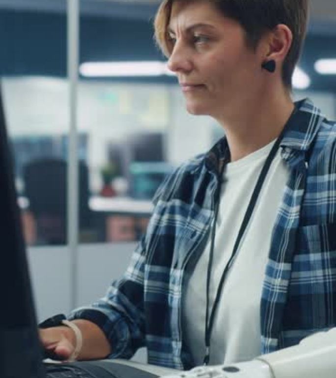 垂直屏幕。在办公室中，有动力的残疾妇女使用假肢在计算机上工作。具有未来思想控制身体动力肌电仿生手的专