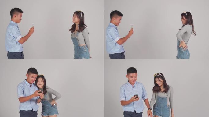 亚洲中国夫妇手牵手走路用手机拍摄照片用灰色背景裁剪