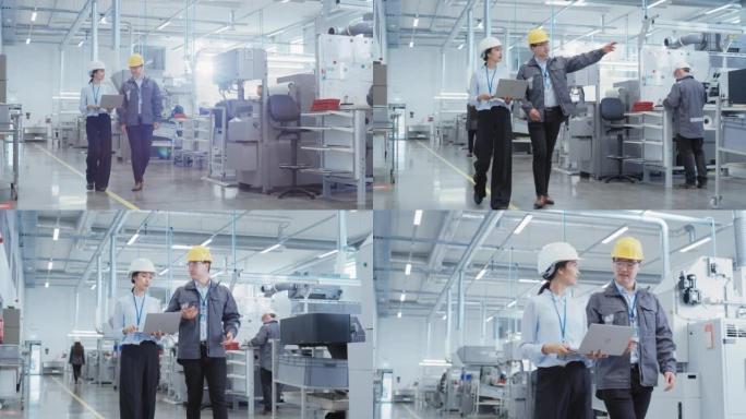 两名戴着安全帽的年轻重工业工程师戴着笔记本电脑走路，在工厂里聊天。两名制造业员工在研发机构工作。