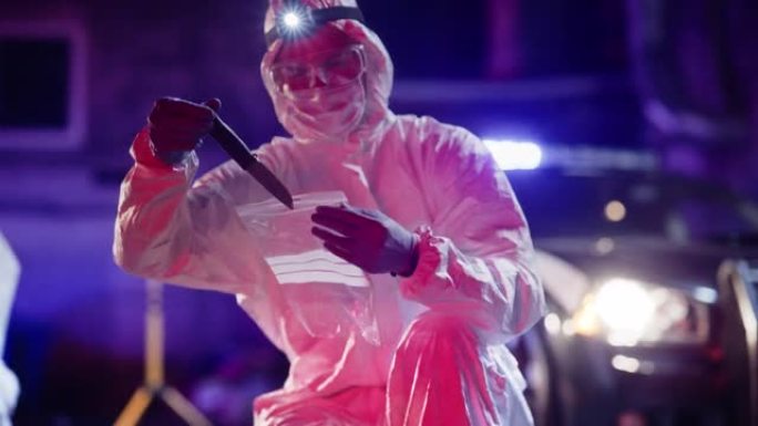 鉴证科专家在犯罪现场找到失踪的凶器。穿着工作服的男子在把刀装进消毒塑料袋作为证据后观察刀上的血迹。
