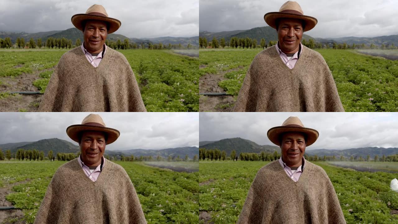 拉丁美洲的男性农民戴着典型的ruana和帽子，在农田里非常高兴地对着相机