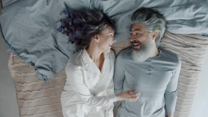 有趣的夫妇跌倒在床上笑然后拥抱和亲吻的高角度视图