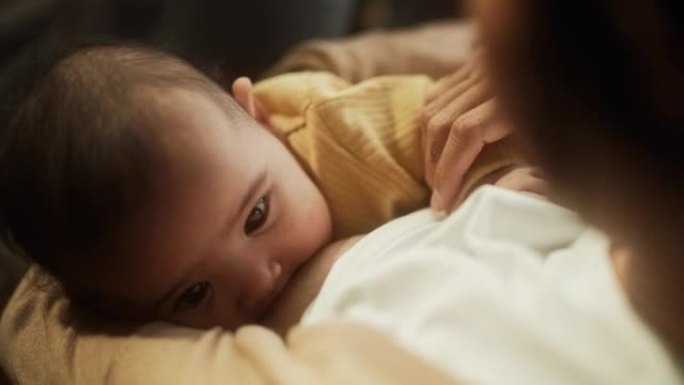 一个可爱的亚洲婴儿从母亲的乳房喂养的高角度肖像。新母亲和婴儿之间的亲密时刻表现出母爱，温柔和无条件的