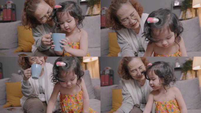 亚洲老人微笑的祖母在家里的客厅里和孙子或孙女一起玩，老年女性开心的同时照顾她的小可爱孩子玩数字平板电
