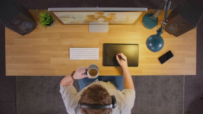 男性平面设计师或带有图形平板电脑的照片润饰的俯视图晚上在创意办公室的电脑上工作，喝咖啡-慢动作拍摄
