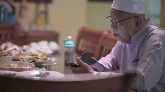马来西亚马来曾祖父坐在餐厅看着他的智能手机检查电话信息