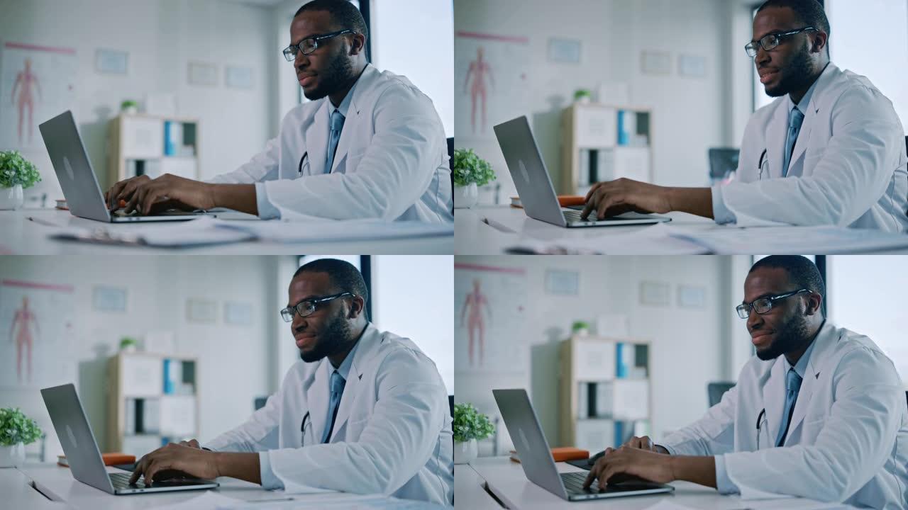快乐的非洲裔美国家庭医生正在一家健康诊所的笔记本电脑上工作。穿着白大褂的医生正在医院办公室的桌子后面