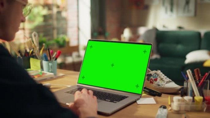 在带有绿色色度键屏幕的笔记本电脑上编码时，使用触摸板查看聚焦男性开发人员的肩膀。远程工作概念的现代自