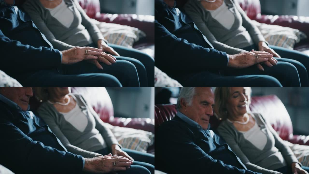 一对可爱的高级夫妇的特写镜头在家里的沙发上牵着彼此的手，深情地表示永远的爱和尊重。