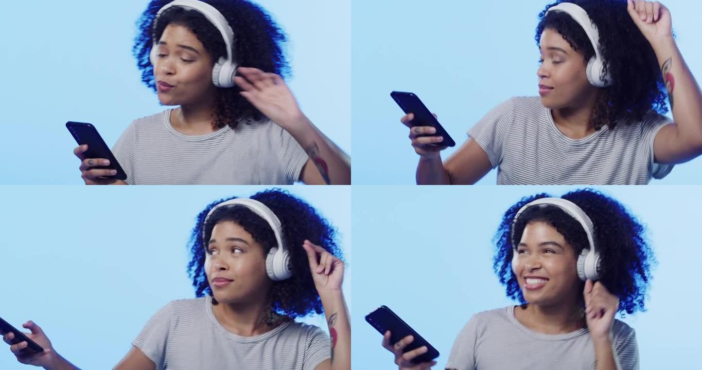 4k视频片段，一个美丽的年轻女子戴着耳机使用手机并在蓝色背景下跳舞