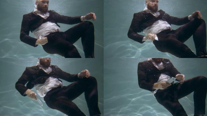 穿着办公室西装的快乐年轻商人的水下电影肖像，从口袋里拿智能手机慢动作。