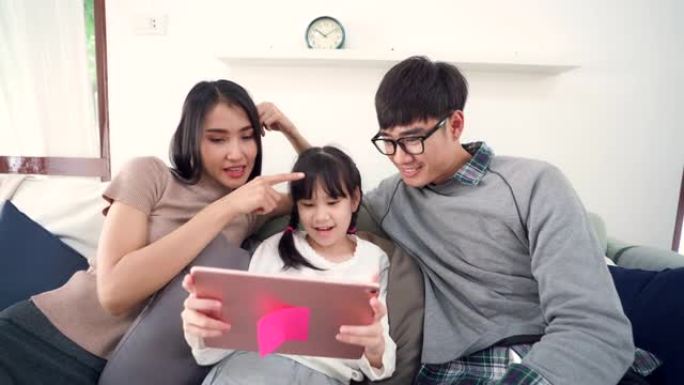 4K UHD掌上电脑: 爸爸妈妈和女儿的快乐亚洲家庭一起在客厅的沙发上看平板电脑。