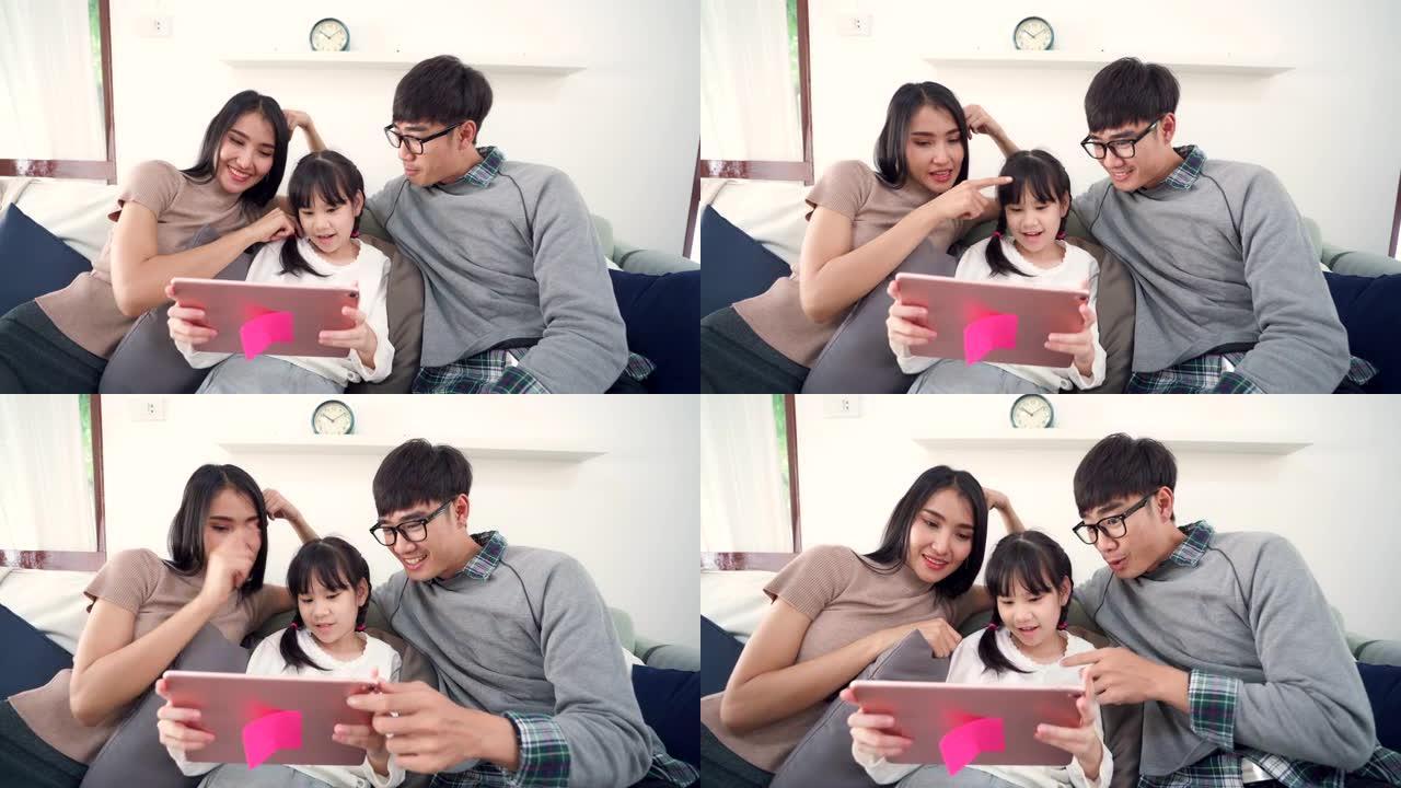 4K UHD掌上电脑: 爸爸妈妈和女儿的快乐亚洲家庭一起在客厅的沙发上看平板电脑。