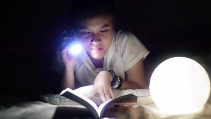 聪明的亚洲女孩在卧室里用手电筒看书