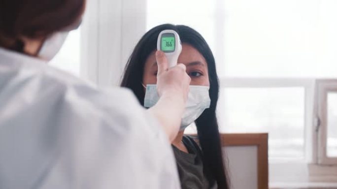 新型冠状病毒肺炎期间检查健康。穿着实验室外套的医生用红外温度计测量混血妇女的温度。