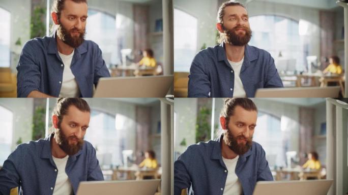 特写一位英俊的长发大胡子经理坐在创意办公室的办公桌前的肖像。时尚的男人在营销公司使用笔记本电脑。撰写