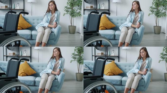 不幸的残疾妇女的肖像独自坐在沙发上，坐着轮椅叹息