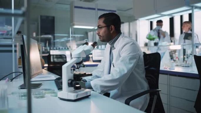 医学研究科学家在显微镜下进行DNA实验，并在生物科学实验室的台式计算机上写下结果。多样化的多民族实验