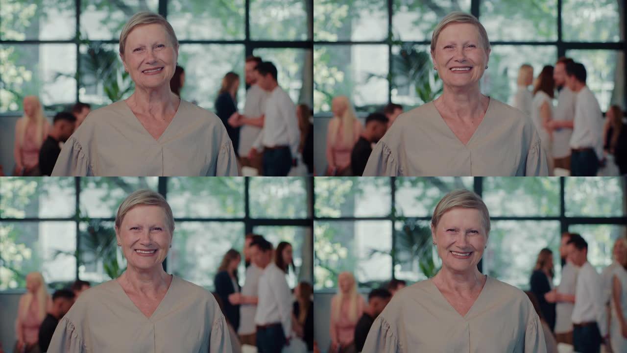 快乐的70多岁白人女商人的肖像看着镜头，对着宽敞繁忙的办公室慢动作微笑。